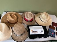 Top-down view of five hats arranged side by side on a white surface, including Panama Jack, vintage Lipoma Firs Gold Club, and others. Black gloves and small leather wallets visible to the right.