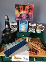 Wide shot showing all items on green desk including steins, vinyl figures, Thermos, tools, speaker mounts, and wooden box