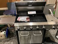 Front view of grill with hood open showing five main cooking grates, control knobs and double-door cabinet below