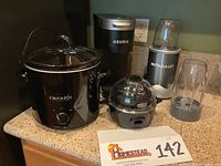 Lot of four electric kitchen appliances: NutriBullet blender, Crock-Pot slow cooker, Keurig coffee maker, Plus Dash egg cooker displayed together on a counter.