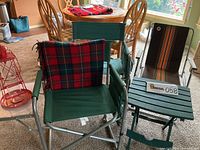 Red metal lighthouse bird feeder, green plastic folding table, green and striped folding chairs with Pendleton throw on green chair.