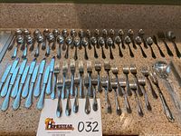Full view of the flatware set arranged on a countertop showing knives, forks, spoons, and serving pieces for quantity verification and condition.
