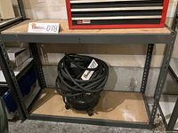 Full view of metal shelving unit with particle board shelves, showing the bottom shelf and part of middle shelf with a tool cabinet on top.