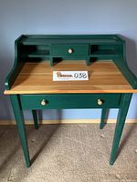 Front view of small forest green painted desk showing natural wood accent top and knobs, with back organizer shelf and drawer.
