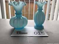 Frontal view of two blue art glass melon vases with ruffled tops on a table with a lot card