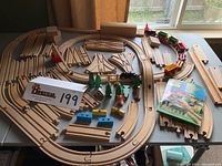 Full layout of vintage Brio wooden railway set on table with wooden track pieces, train cars, trees, signs, and manual booklet visible.
