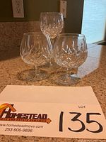 Three Waterford Lismore crystal stem glasses on granite countertop with lot number tag. Two shorter brandy stems and one taller wine stem.