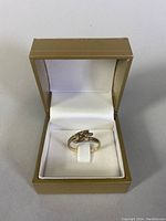 Ring displayed inside gold-tone ring box viewed at front angle