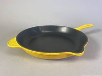 Side view of the yellow Le Creuset skillet showing the black enamel interior and yellow exterior.