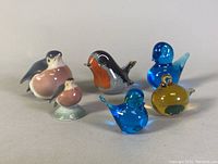 Five bird sculptures together, two porcelain with pastel colors and three glass birds in blue and amber hues