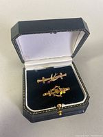 Two rose gold brooch pins displayed on black velvet inside a hinged box