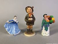 Three porcelain figurines shown together on neutral background: blue dress dancer, child with balloons, girl in cloak with basket