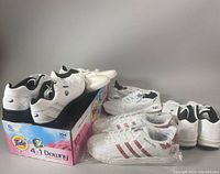 Five pairs of mostly white running shoes arranged on a box, showing Adidas Mercedes-Benz pair in front.