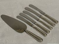 All six pieces laid out on a cloth: one large cake cutter and five smaller spreaders showing handles and blades.