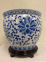 Front view of the large blue and white porcelain planter pot on wooden base showing floral and vine decoration.