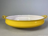 Side view showing yellow enamel exterior with integrated handles and white interior.