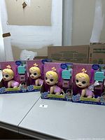 Four Baby Alive dolls in original boxed packaging shown on a table with a plain wall background