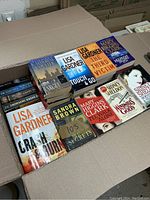 Top view of cardboard box filled with bestselling author books stacked neatly and visible titles.
