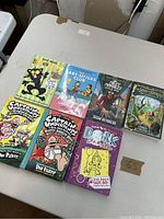 Photo showing seven bestselling teen books arranged on white table including Bad Kitty, Baby-Sitters Club, Captain Underpants series, Dork Diaries, Long Way Down and The Land of Stories