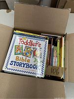 Photo showing open cardboard box filled with assorted children's books, with Toddler's ABC Bible Storybook on top