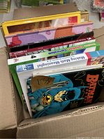 Top view of 8 children's books visible in a box, including math, grammar, language, and a Batman comic book.