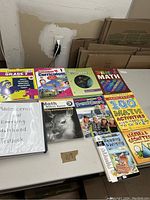Photo showing 9 various educational books arranged on a table including math, reading, and curriculum workbooks along with a textbook in a white binder