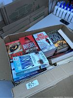 Photo of a box containing multiple James Patterson books stacked together including titles Zoo, Invisible, Swimsuit, The Family Lawyer and others.