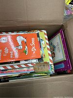 Top view of a box filled with various children's books including a visible copy of 'Green Eggs and Ham' by Dr. Seuss.