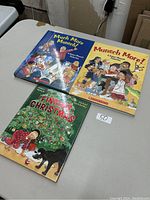 Three hardcover children's books on a table: 'Much More Munsch!' with a blue cover, 'Munsch More!' with a yellow cover, and 'Finding Christmas' with a Christmas tree and black dog on the cover.