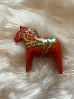 Front and side views of the hand painted red wooden Dalecarlian Horse with traditional Swedish decorative motifs on white furry background.