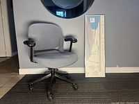 Herman Miller Equa desk chair and James Harill framed print positioned beside each other against a gray wall on dark carpet.