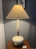 Full view of the lamp lit, showing the silhouette, base, neck, and shade with the lamp on a wooden surface.