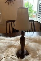 Front view of the lamp on a table showing the full lamp with wooden base and fabric shade.