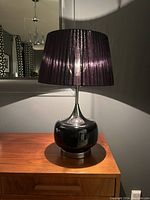 Full table lamp with chrome and ceramic base on wooden surface, shade lit from behind.