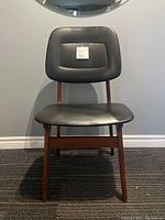 Front view of the teak wood framed chair with black upholstered seat and backrest showing typical mid century modern style and finish.