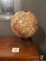 Side view of the postmodern world globe showing Africa, Europe, and part of Asia with wooden base in front of gray wall.