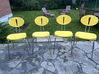 Front view of all four yellow HOLA-OLA chairs showing oval backrests with vertical cutouts and tubular metal legs.