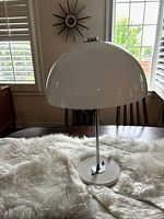 Front view of the mushroom lamp on a fluffy white surface showing the large white dome-shaped acrylic shade and chrome stand.
