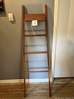 Full front view of the leaning teak ladder against a gray wall.