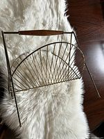 Side view of the vintage brass magazine rack showing its fan-like wire design, angled legs, and wooden handle.