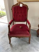 Front angle view of wooden framed arm chair with red velvet upholstery showing top carved wood detail and tufted backrest.