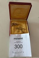 Red display box with gold interior holding two gold bracelets, label shows 14K gold mark.