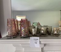 Photo showing 2 tall candle holders with iridescent pink mosaic glass covers and 4 metal holders with ribbed clear glass covers on a mantle