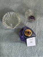 Crystal ball lighter, clear shell-shaped crystal tray, and small clear glass bowl with purple base on grey carpet.