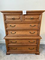 Front view of the six drawer wooden dresser showing brass handles and ring pulls on drawers and the overall wood finish.