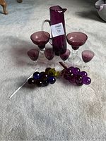 Full set including purple glass pitcher, stirring stick, four cordial glasses, two bubble martini glasses, and two acrylic grape decor pieces all arranged on carpeted floor.