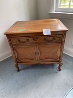 Front view of end table showing drawer with brass handles and cane style bottom cabinet doors.