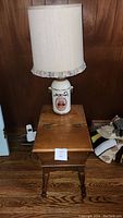 Full view of wooden end table with hinged top and ceramic lamp on top