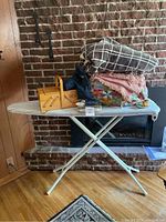 Ironing board with various items on top including folded blankets, wooden sewing box, and sewing accessories.