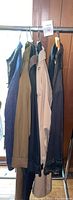 Four men's outerwear items hanging on rack: tan/beige, black, dark colors; various styles including trench and casual jackets.